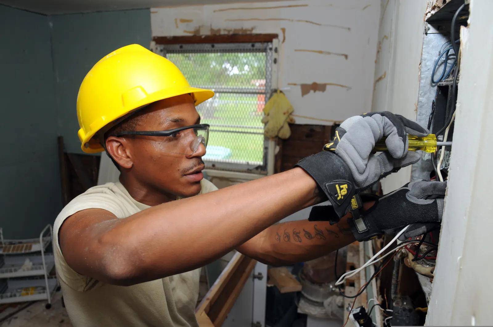 Technicien intervenant sur un tableau électrique, équipé de gants et de lunettes de protection